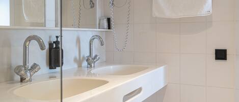 A modern bathroom with a large sink, two faucets, a mirror, a towel rack, and a toilet.