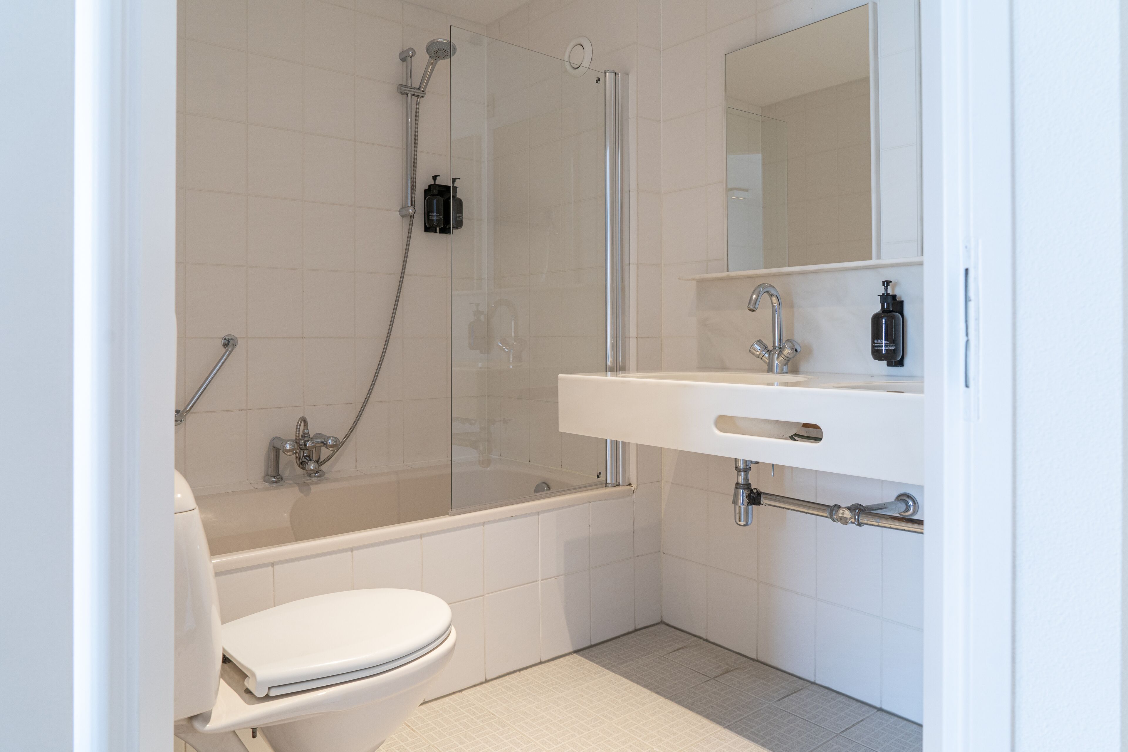 Une salle de bain moderne avec une douche à parois de verre, des toilettes blanches et un lavabo avec un miroir au-dessus.