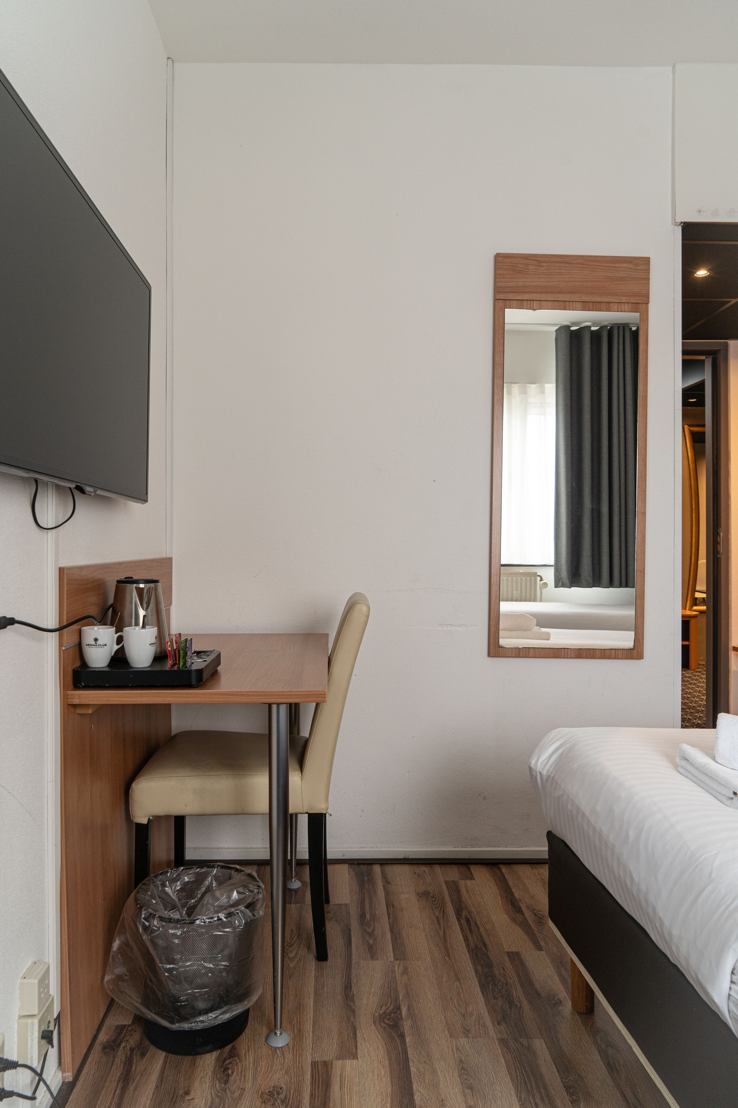 Une chambre d’hôtel équipée d’un lit, d’un bureau avec une machine à café, d’une chaise, d’une poubelle et d’un téléviseur fixé au mur.
