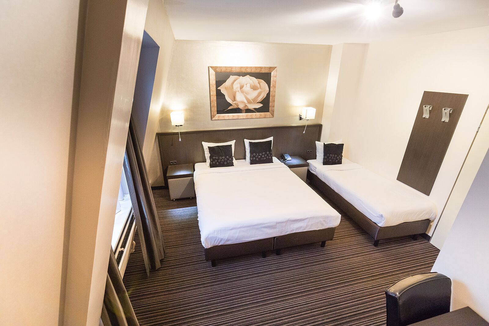 Ein Hotelzimmer mit zwei Einzelbetten, einem großen gerahmten Kunstwerk an der Wand, Nachttischlampen, einem kleinen Tisch und einem Stuhl.