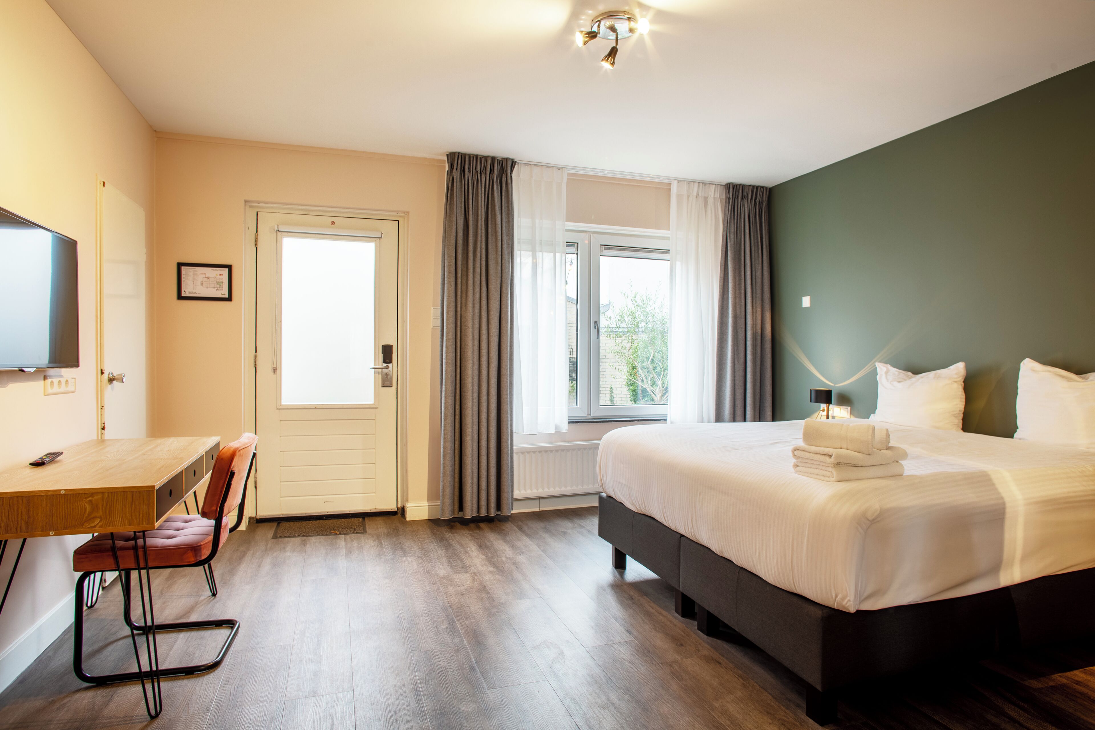 Une chambre d’hôtel équipée d’un lit, d’un bureau, d’une chaise, d’une télévision et d’une fenêtre avec des rideaux.