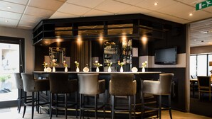 A bar area with a counter, multiple bar stools, a television mounted on the wall, and a mirror above the counter.