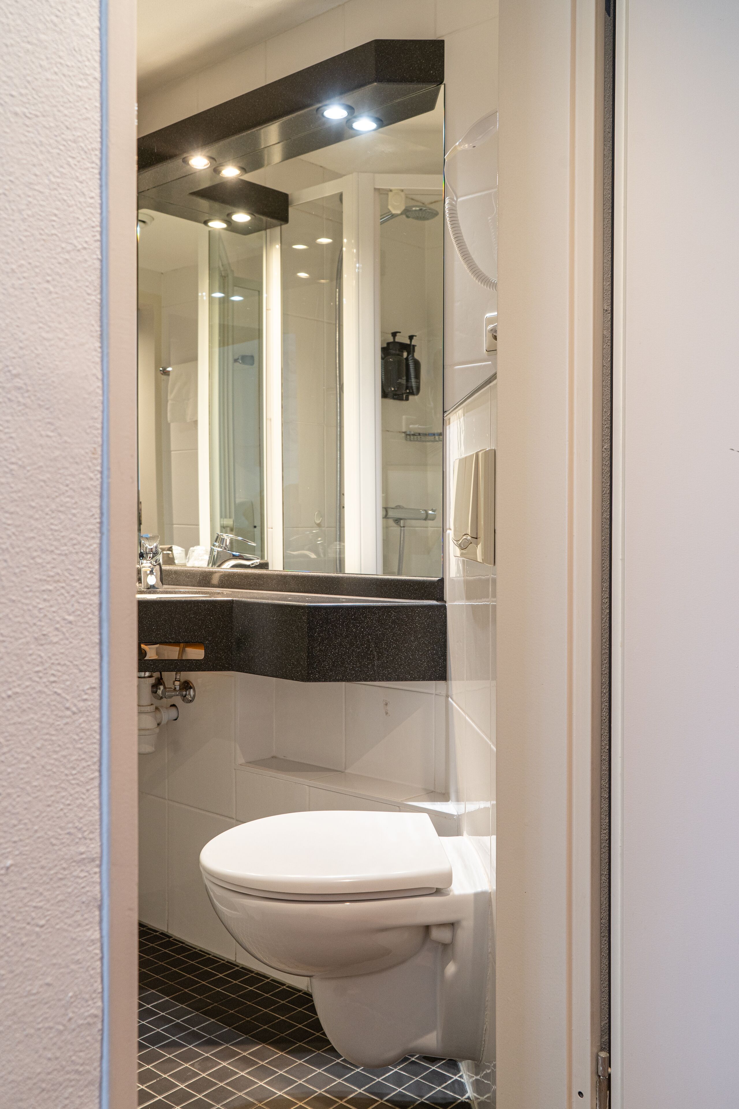 A modern bathroom with a white toilet, a black countertop, and a mirror above the sink.