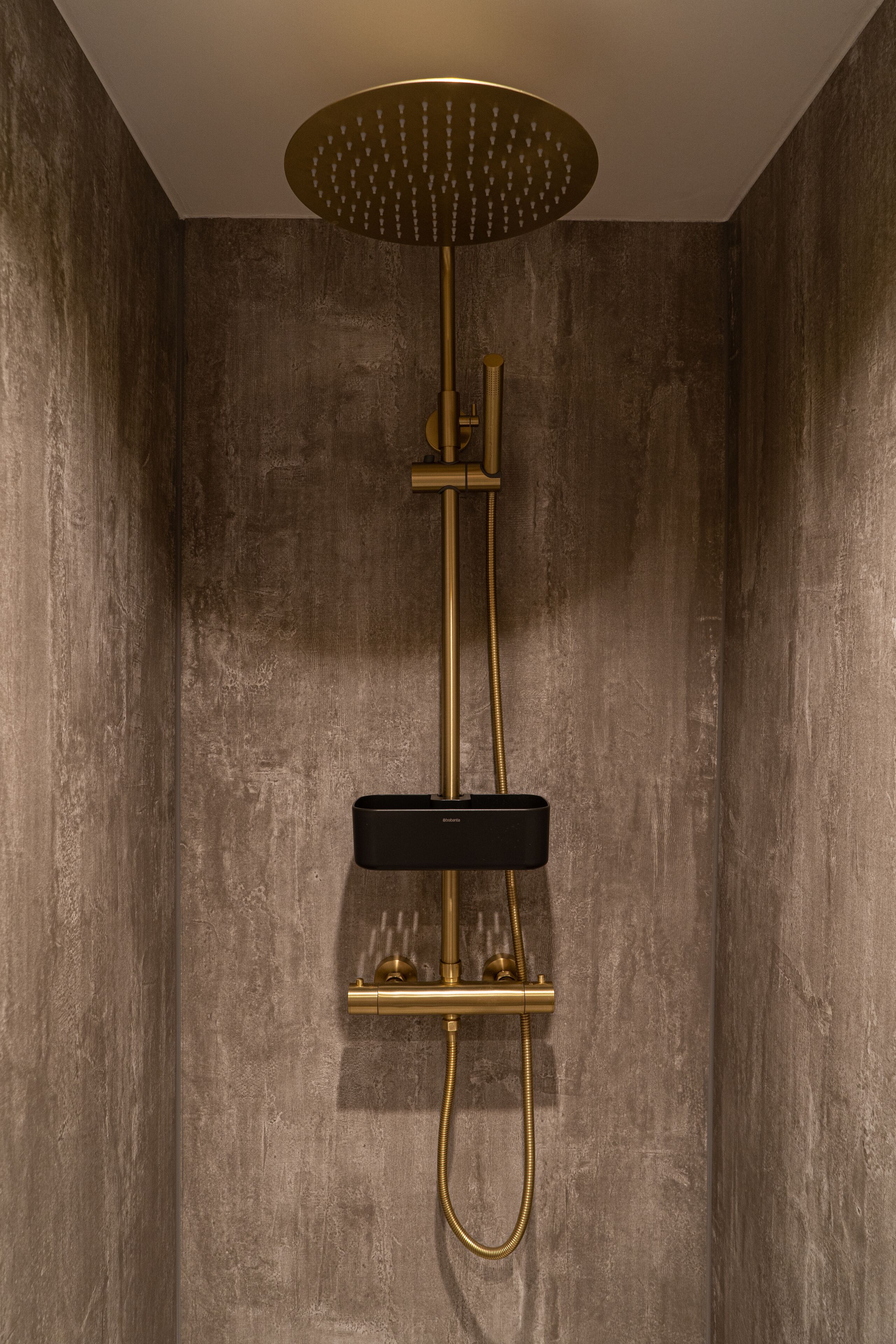 A modern shower with a gold finish, a circular overhead showerhead, and a handheld showerhead.