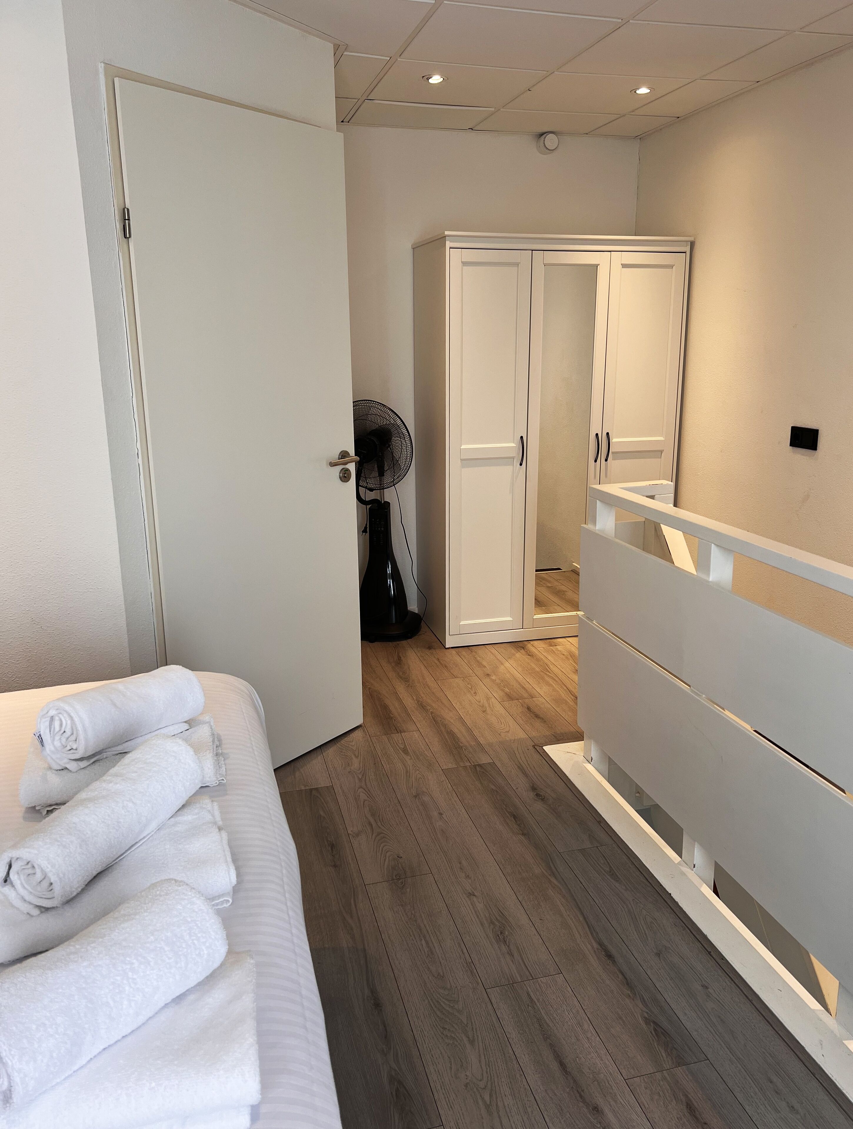 Una habitación de hotel con cama, armario, ventilador y una puerta que da a otra habitación.