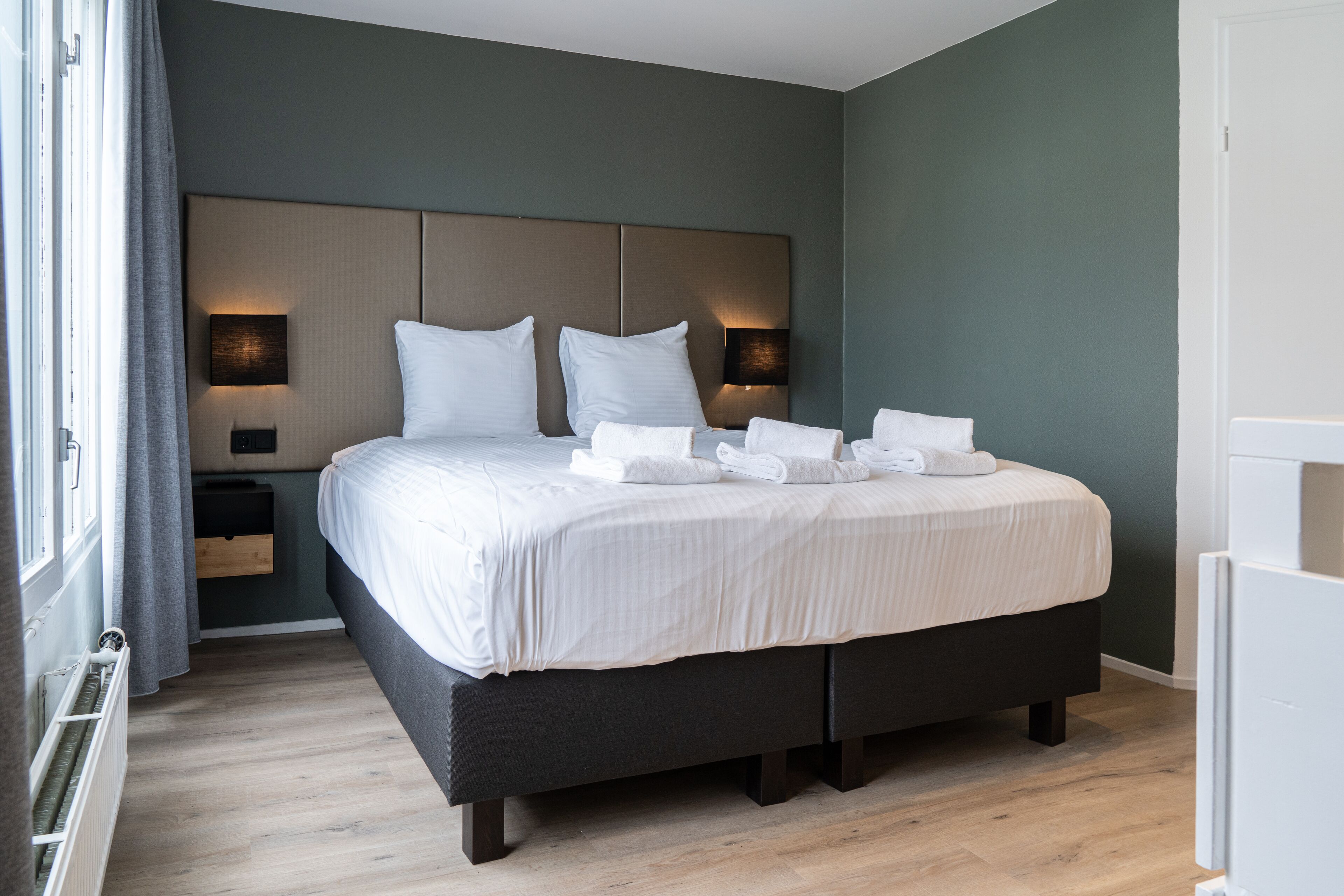 Quarto de hotel moderno com uma cama grande, luminárias laterais e aquecedor embutido.