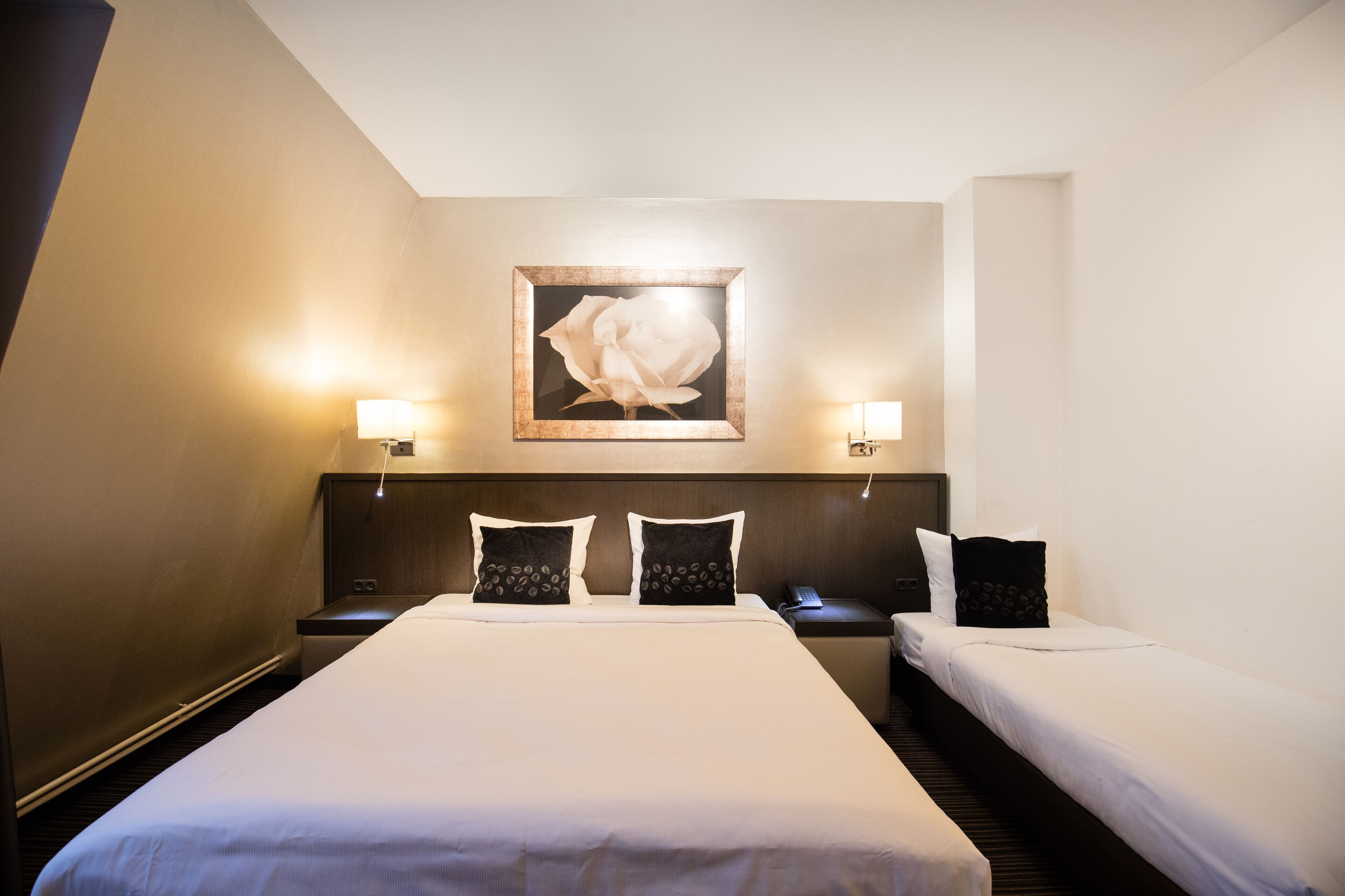 A hotel room with a large bed, two bedside tables, a nightstand, and a framed artwork on the wall.