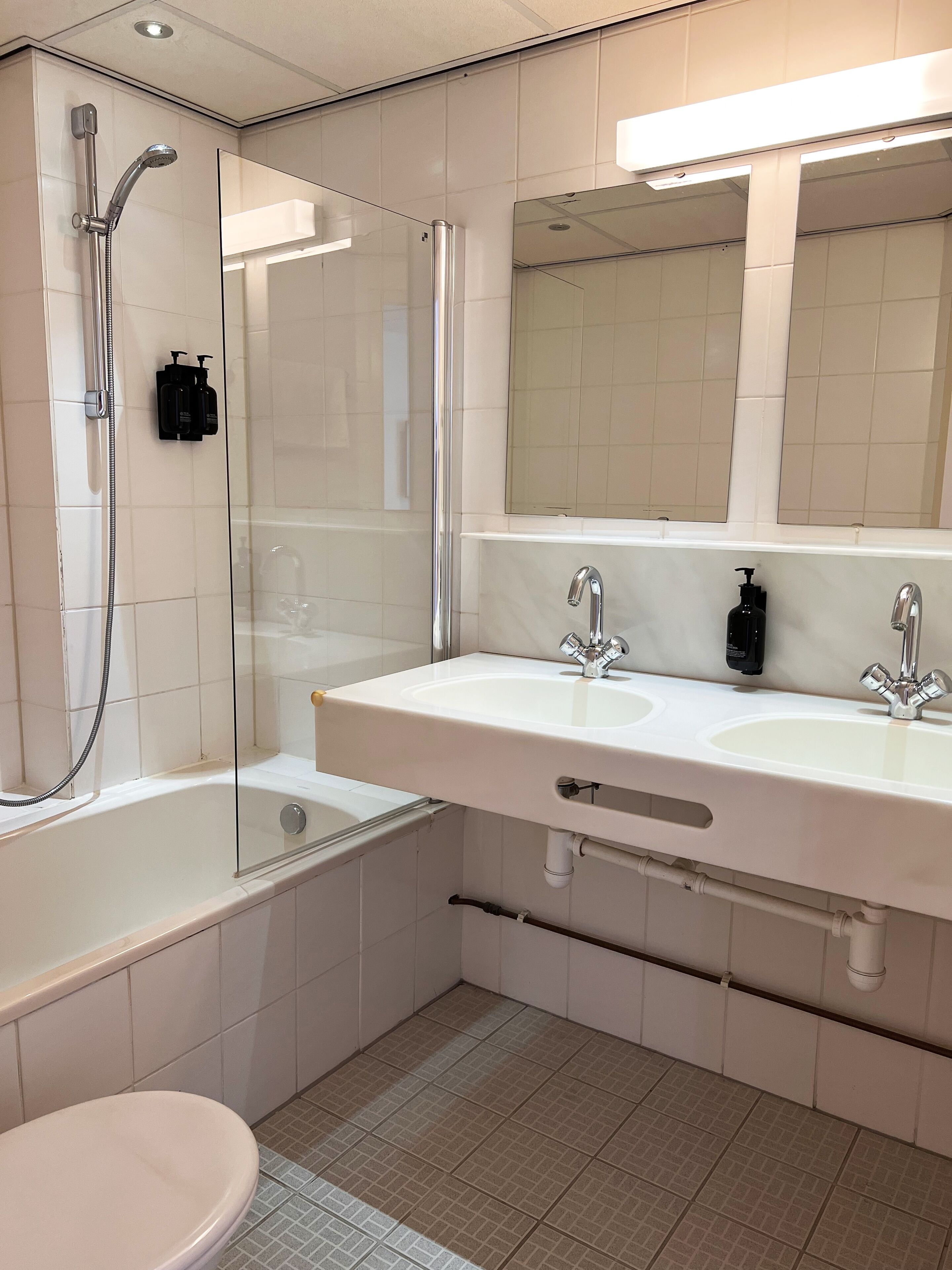 A modern bathroom with a glass-enclosed shower, a double sink with a mirror above, and a toilet.