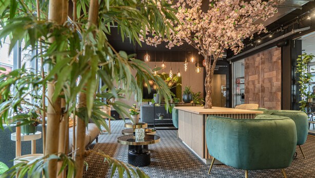 A modern interior with a reception desk, green upholstered seating, and a decorative tree with pink blossoms.