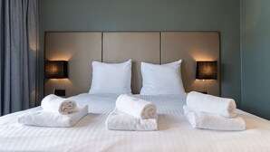 A neatly made bed with white linens and two rolled towels on the side.