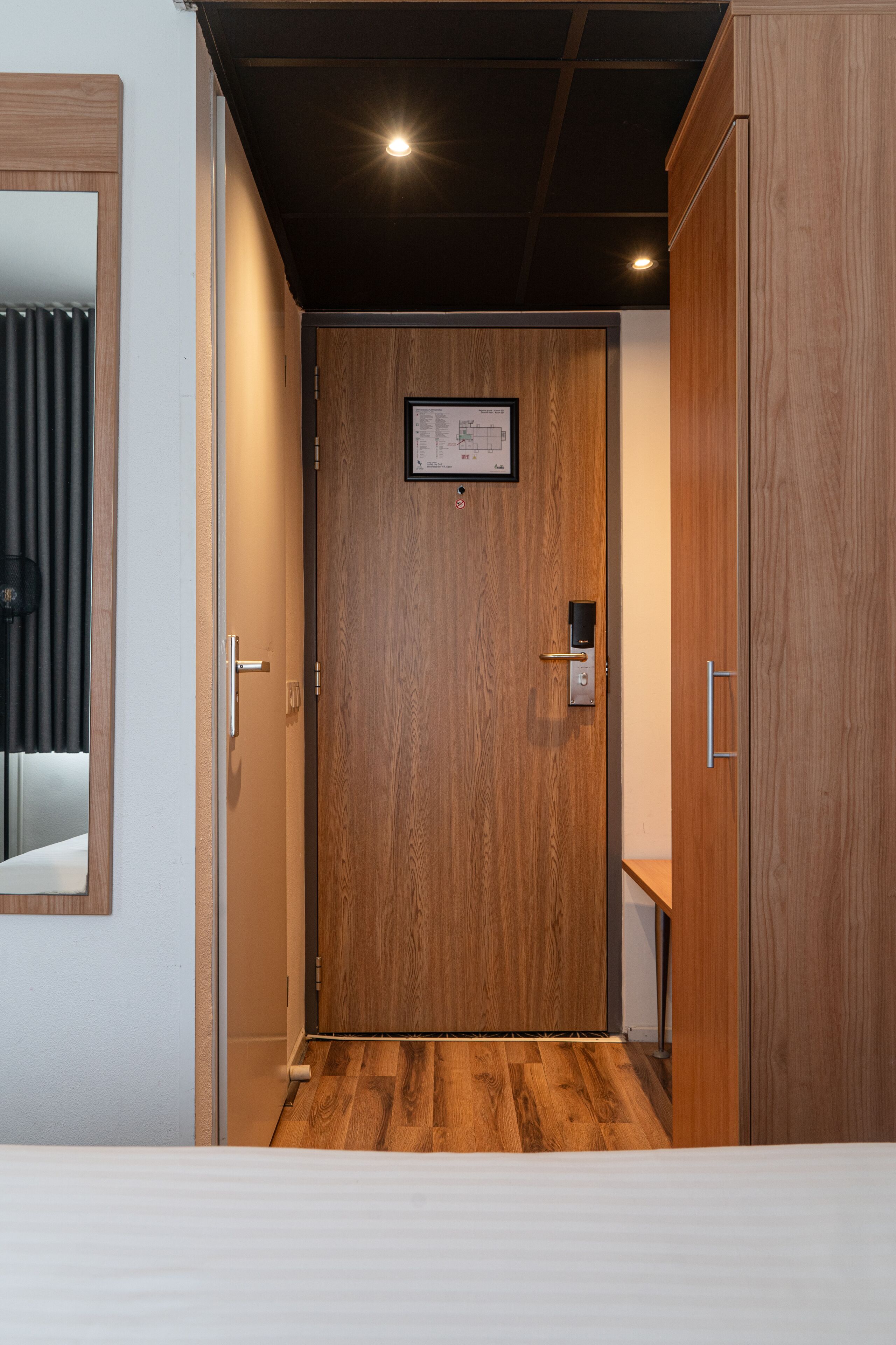 A wooden door with a keyhole and a small plaque, a wooden floor, and a white wall with a mirror.