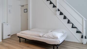 Un dormitorio con una cama, una puerta blanca, un electrodoméstico pequeño y blanco, y una escalera con escalones blancos y negros.
