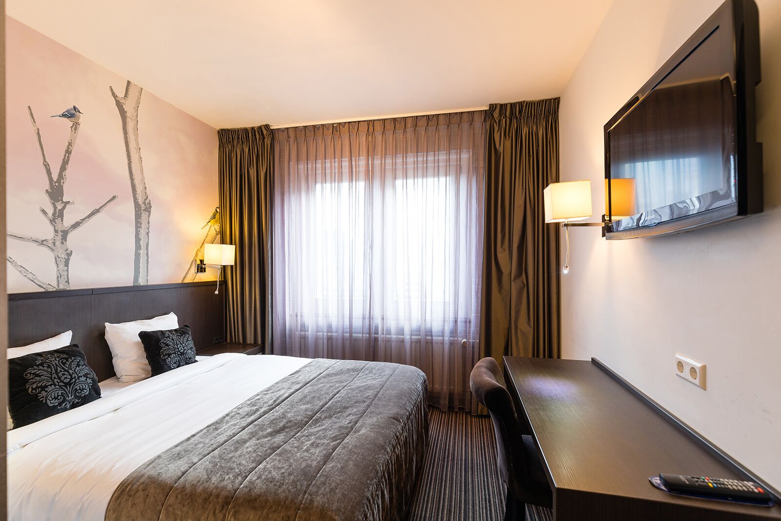 Une chambre d’hôtel avec un grand lit, un bureau, une télévision et une fenêtre avec des rideaux.