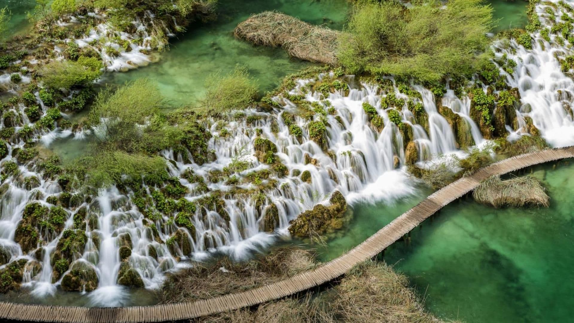 A waterfall cascading over moss-covered rocks with a wooden viewing platform.
