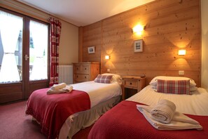 A hotel room with two beds, wooden paneling, and a window with curtains. - Hotel Christiania (Les Gets)