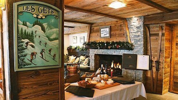 Um interior rústico com teto de madeira, lareira de pedra e uma mesa com comida e bebidas.