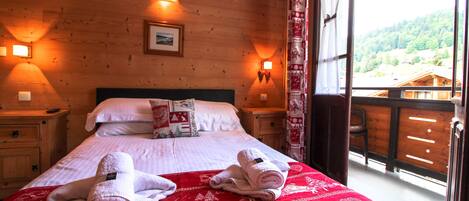 Una habitación de madera con una cama, dos lámparas de noche y vistas a un bosque.