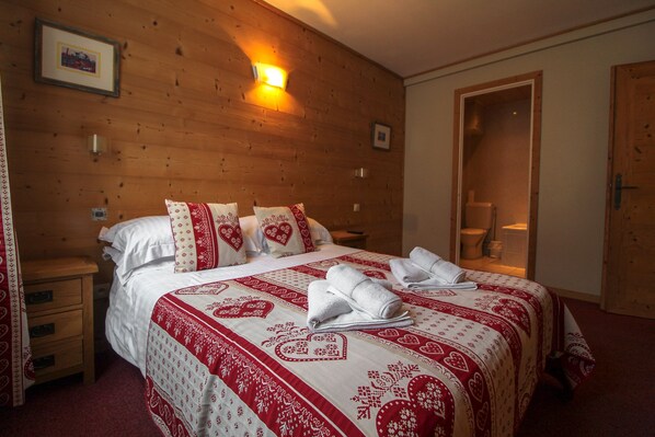 A neatly made bed with a red and white patterned bedspread, a wooden headboard, and a nightstand with a drawer. - Hotel Christiania (Les Gets)