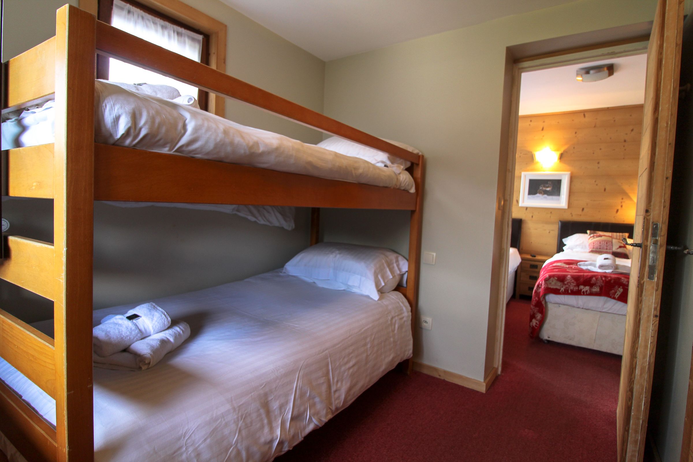 A bunk bed room with a red carpet, a wooden door, and a framed picture on the wall.