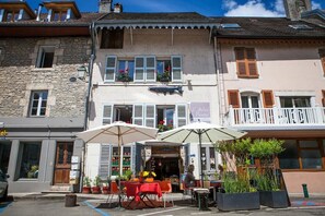 A building with a restaurant on the ground floor, featuring outdoor seating with umbrellas and potted plants. - Chambres d'Hôtes l'Atelier du Peintre (Ornans)
