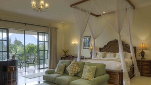 Un dormitorio con cama con dosel, una zona de estar con sofá y un balcón con vistas a zonas verdes.