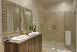 Un baño moderno con tocador doble, un espejo grande y zona de ducha con mampara de cristal.