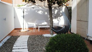Eine Terrasse mit einem weißen Tisch, zwei weißen Stühlen, einem Hängesessel und einem kleinen Busch.