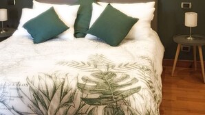 Ein Bett mit Bettwäsche mit Pflanzenmuster, zwei grüne Kissen und je eine Nachttischlampe auf beiden Seiten.