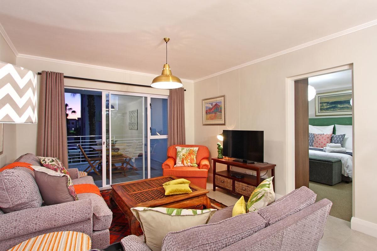 A living room with a sofa set, a television, a coffee table, and a sliding glass door leading to a balcony.