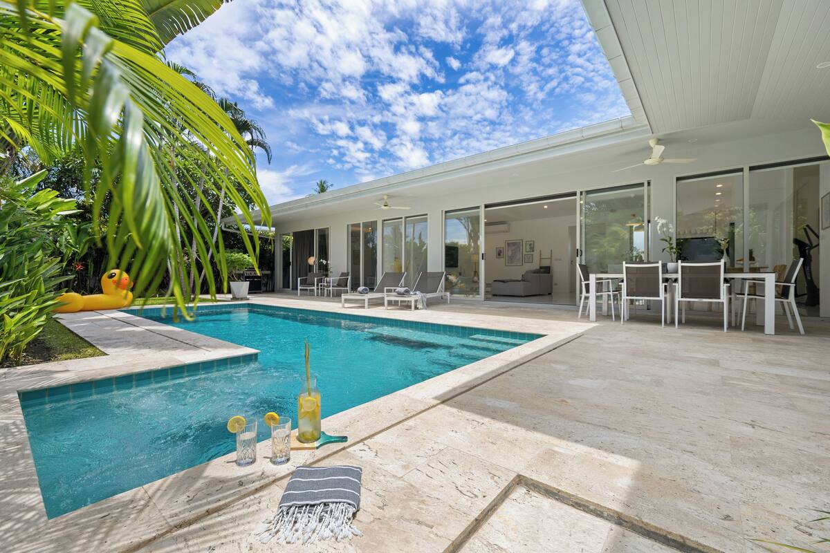 Ein moderner Poolbereich mit blauem Himmel, einer Lounge mit Sesseln und einem Essbereich mit Tischen und Stühlen.