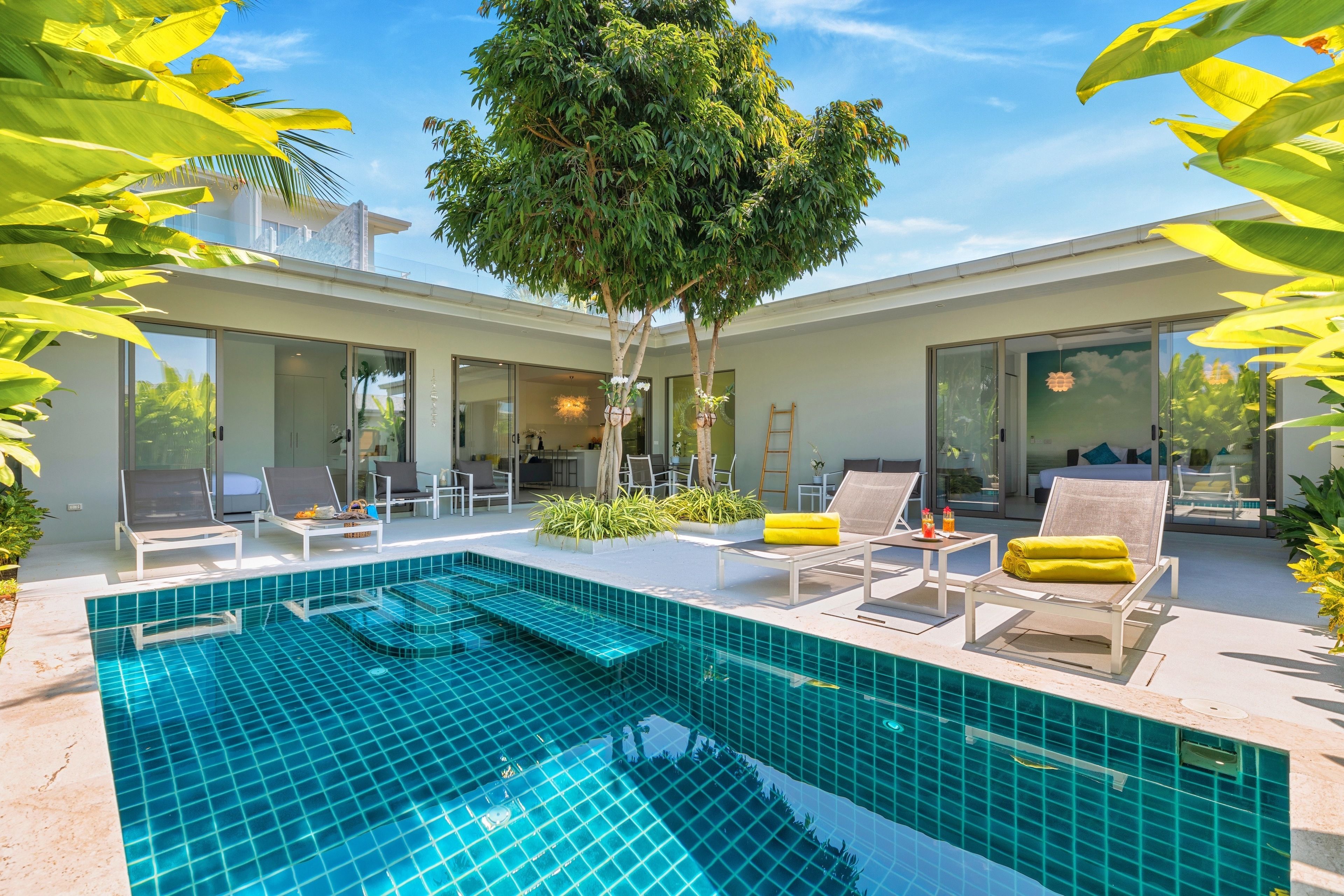 A modern outdoor pool area with lounge chairs, a tree, and a clear blue sky.