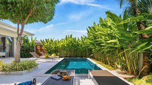 Uma área de piscina privativa com espreguiçadeiras, uma pequena mesa com bebidas e vegetação tropical exuberante.