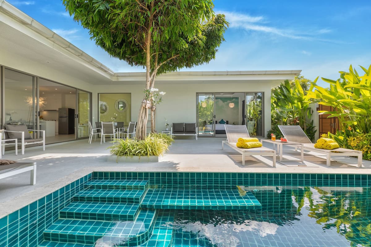 Ein modernes Haus mit Swimmingpool, Sitzgelegenheiten im Freien und einem großen Baum.