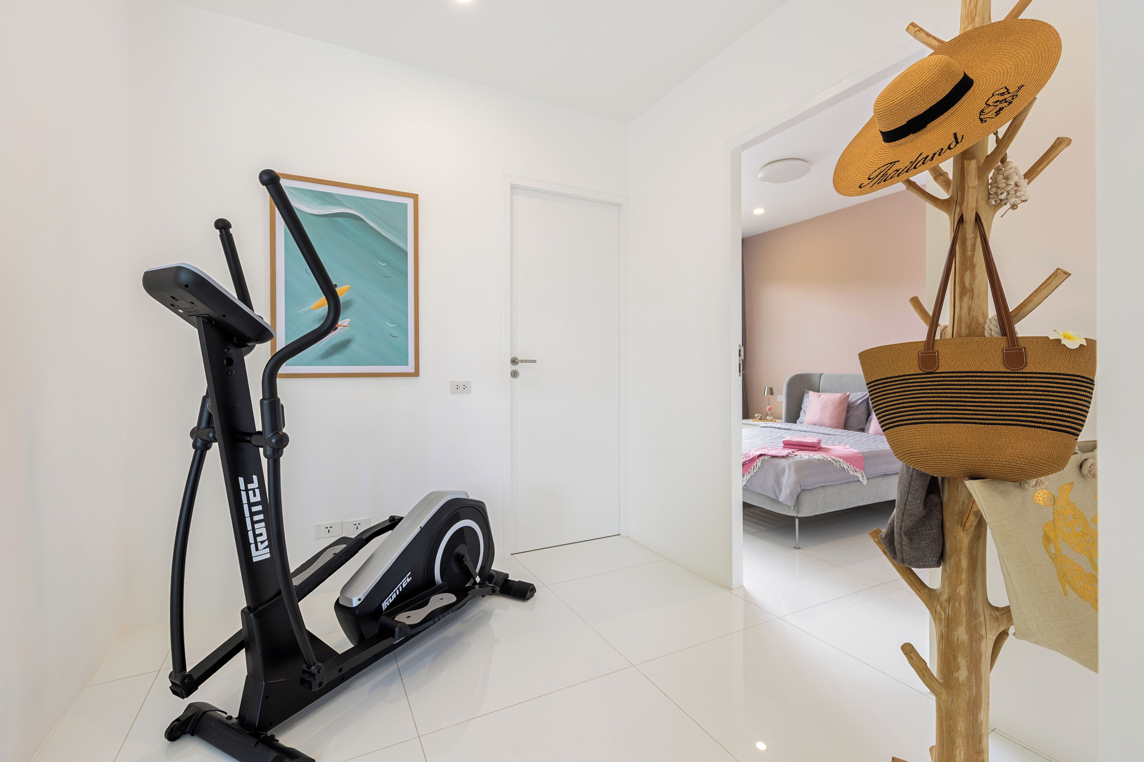 A modern living room with a stationary bike, a framed artwork, and a wooden stand holding a hat and a woven basket.