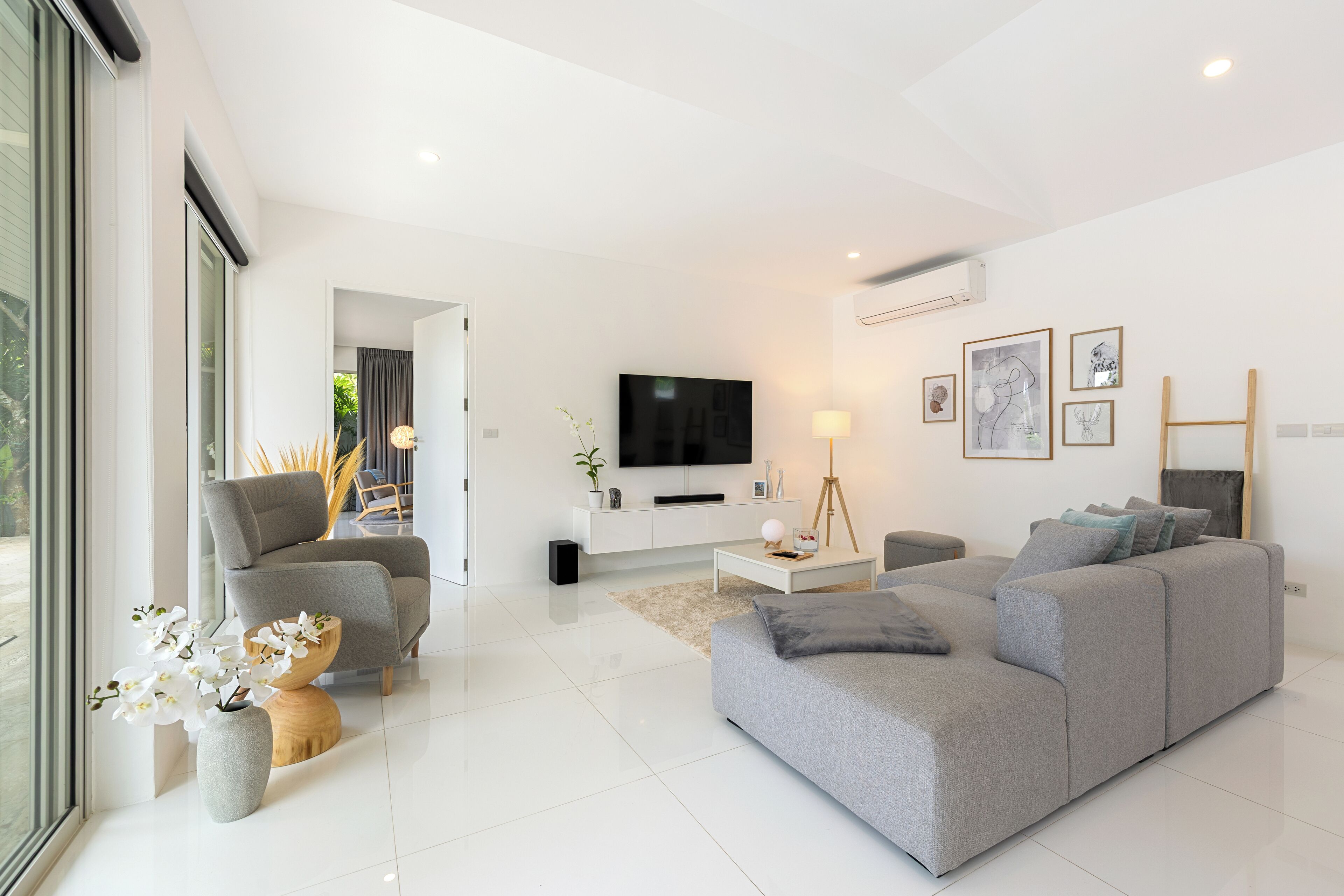 Un salon moderne avec un canapé gris, une table basse blanche et un téléviseur à écran plat fixé au mur.
