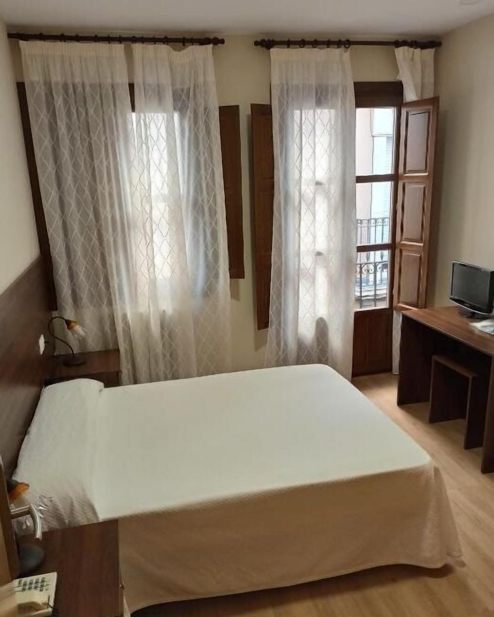 A hotel room with a bed, a desk, a television, and a window with curtains.