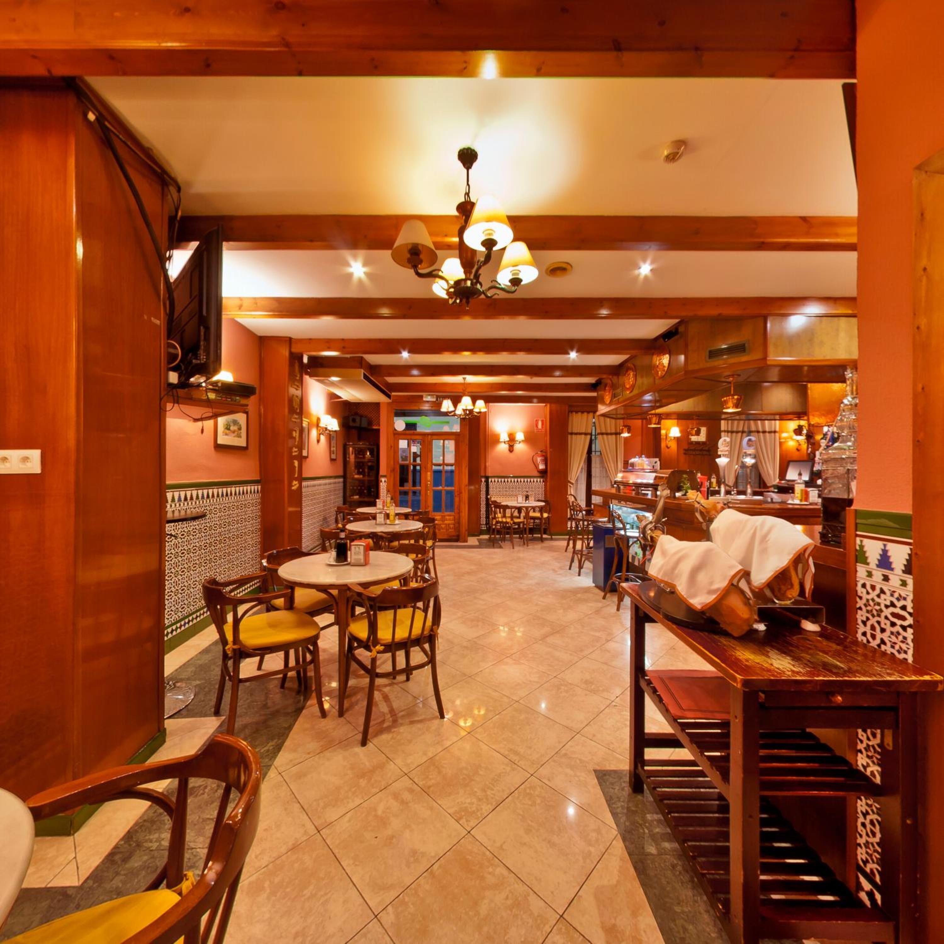 A restaurant with wooden interiors, tiled floors, and multiple dining tables and chairs.