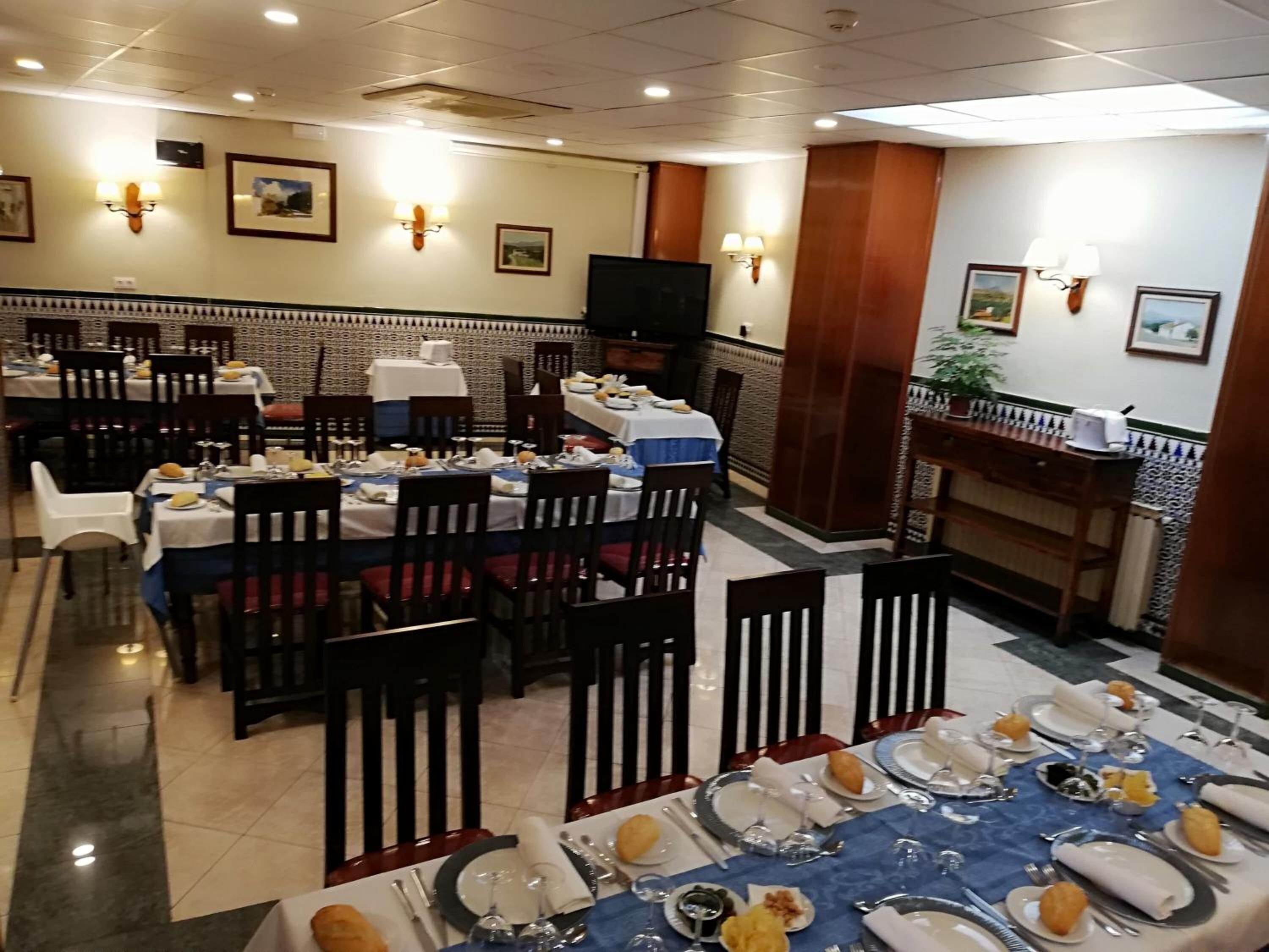 A dining area with multiple tables set for meals, chairs, and wall-mounted light fixtures.