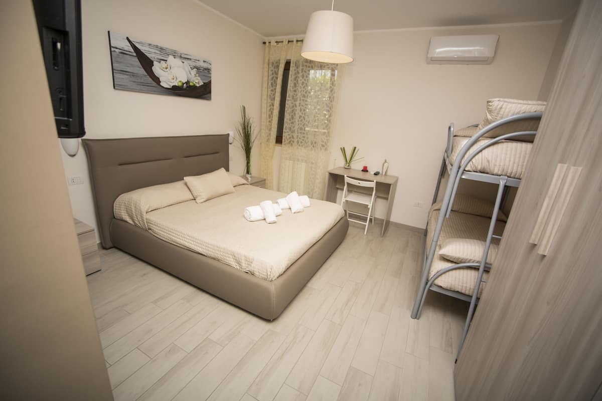A bedroom with a bed, a desk, a chair, a bunk bed, and a window with curtains.