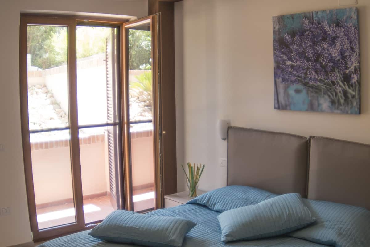 A bedroom with a bed, a hanging lamp, a painting, and a sliding glass door to the outside.