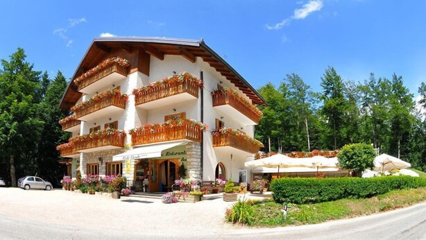 A multi-story hotel with balconies adorned with flowers, a stone facade, and a welcoming entrance. - Albergo Nido Verde (Lavarone)