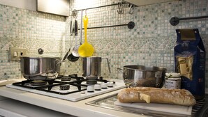 Uma cozinha com fogão a gás, panelas, um escorredor e uma baguete sobre o balcão.