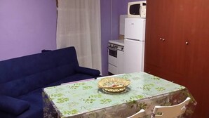 A small room with a blue sofa, a table with a basket, a white refrigerator, and a wooden door. - Relais des Alpes (Giaglione)