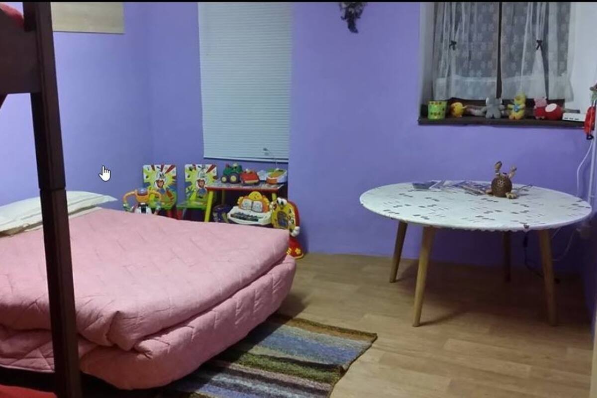 A room with a bunk bed, a small table with a decorative item, and a window with curtains.