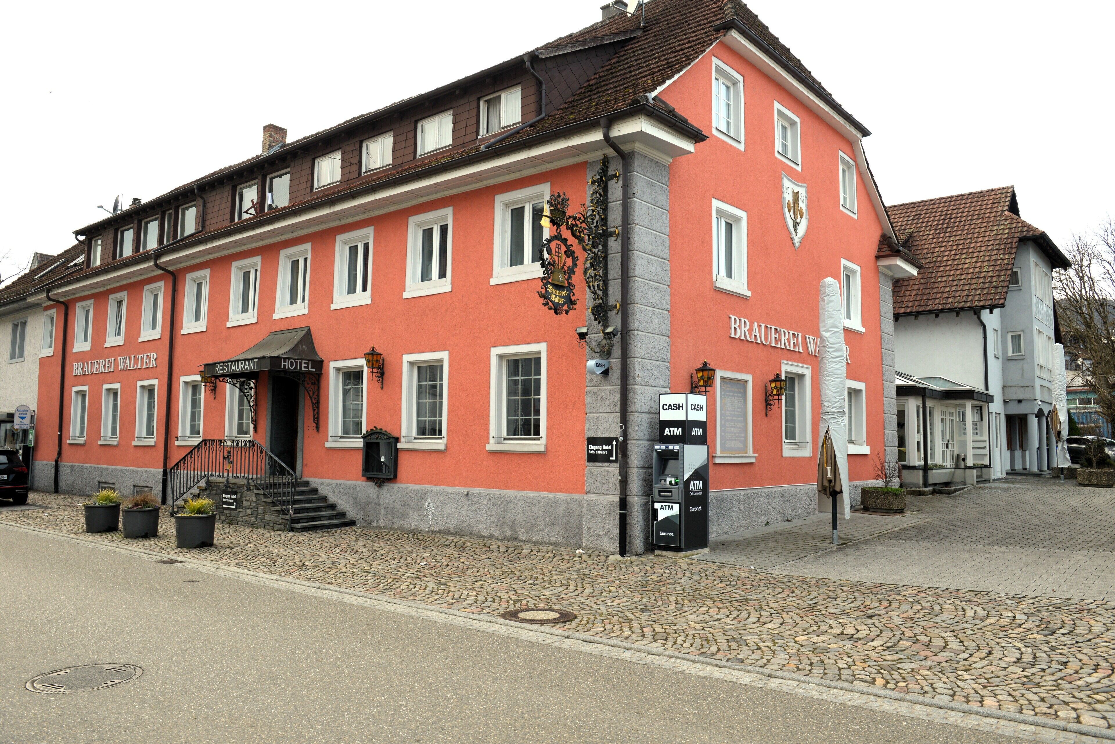 A red building with a sign reading "BRAUERWEI HOTEL" and an ATM on the ground floor.