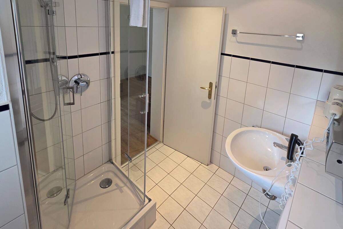 Un baño moderno con ducha de vidrio, lavamanos blanco y retrete.