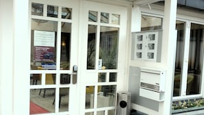 En byggnad med en vit fasad, stora glasdörrar och en metallbehållare för sopor utanför.