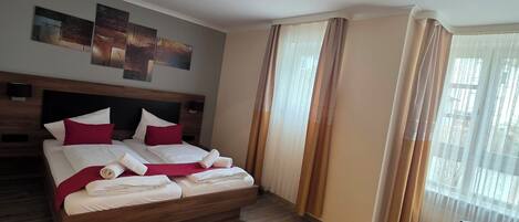 A hotel room with a wooden bed, a desk, a ceiling light, and a window with curtains.