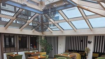 Ein moderner Innenraum mit Glasdecke, Holztischen und grünen Stühlen.