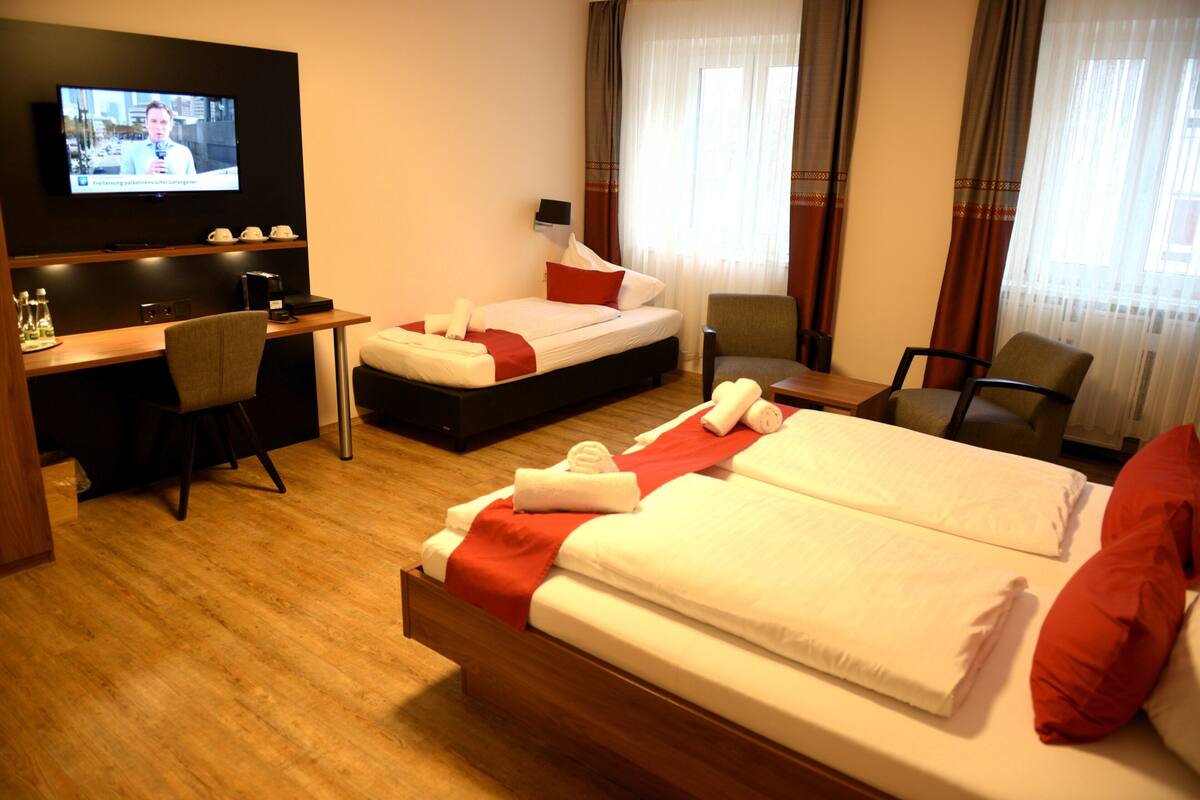 Habitación de hotel con cama, escritorio, silla, televisor y ventana con cortinas.
